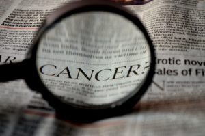 Early Diagnosis. The word cancer under a magnifying glass on a newspaper.